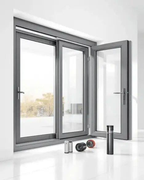 Moderna finestra con cornice grigia e un pannello aperto; tre piccoli cilindri metallici sono posizionati sul pavimento bianco vicino alla finestra. {{brizy_dc_image_alt imageSrc=